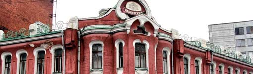 Красное кирпичное здание с арочными окнами и декоративным фронтоном, на котором видна надпись «Красный Октябрь» в круглой рамке.