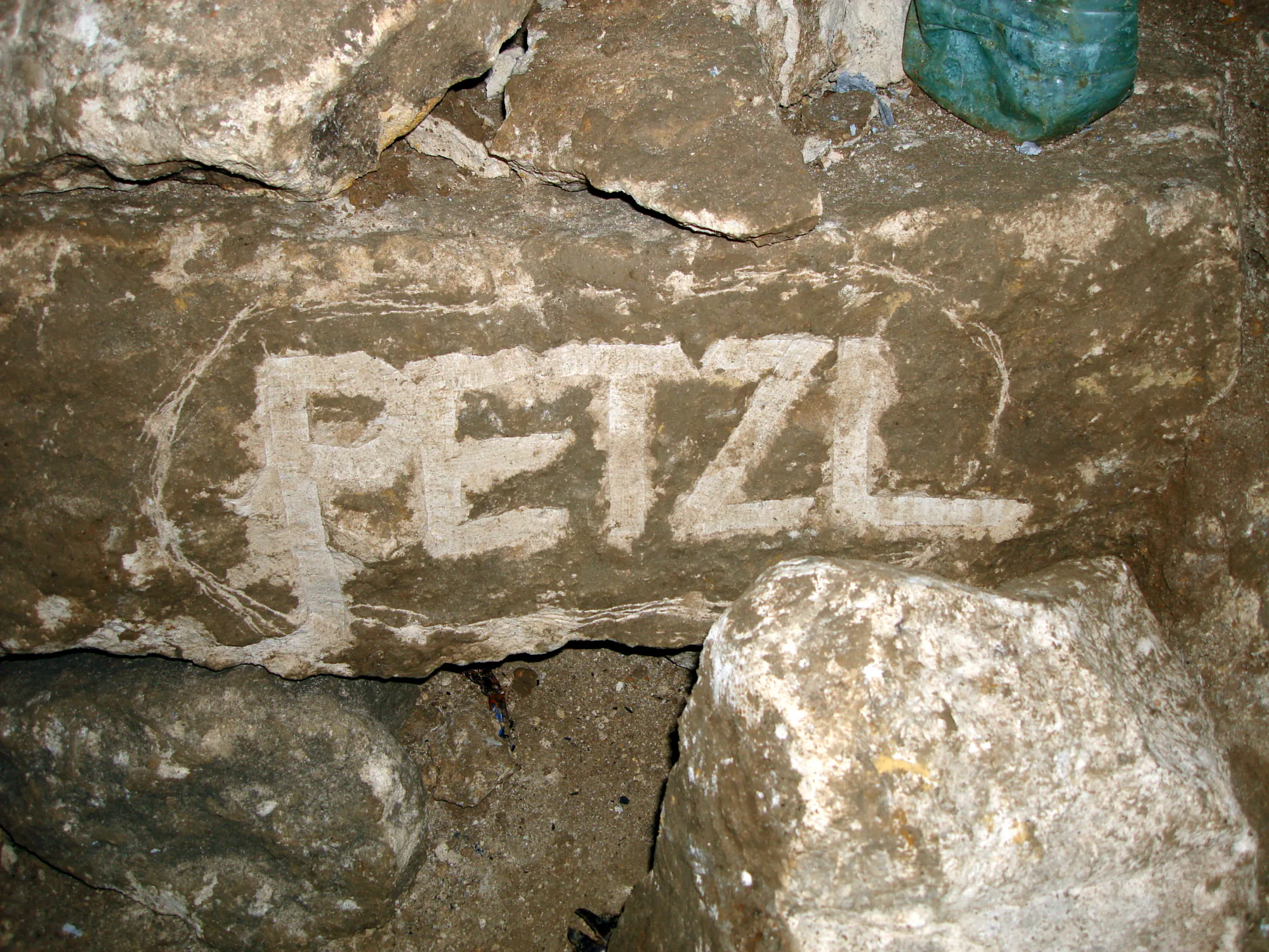 Надпись «PETZL» белым цветом на грубой каменной поверхности, вероятно, в пещере или подземном сооружении.