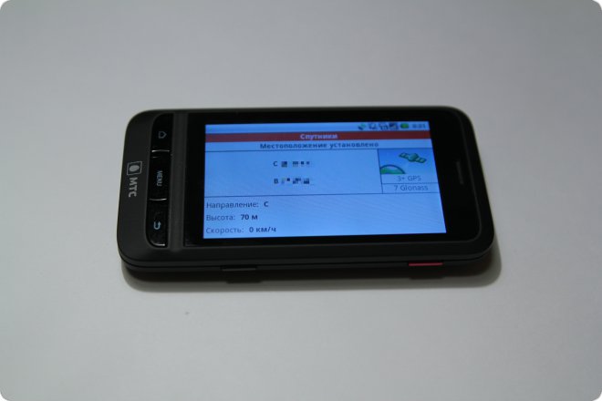 Смартфон МТС на белом фоне: экран показывает GPS-навигацию — направление С, высота 70 м, скорость 0 км/ч, подключено 7 спутников Glonass.