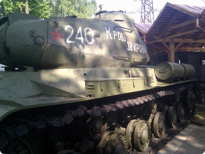 Зелёный танк с красной звездой, надписью «240 К РОВЬ ЗА КРОВЬ» и бочкой на броне, стоит под навесом на открытом воздухе.