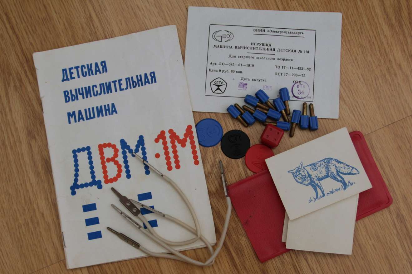 Детская вычислительная машина ДВМ-1М: инструкция, карточки с рисунками, синие и красные детали, щупы, документ ВНИИ «Электронстандарт» на деревянном столе.
