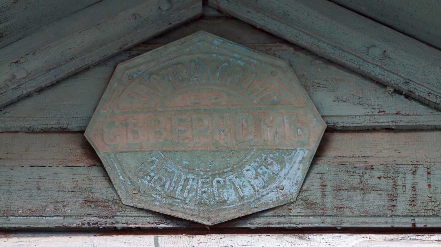 Потёртая металлическая табличка в форме восьмиугольника с надписью «СЕВЕРНОМ» и «РЕМОНТ СТРОИТЕЛЬНЫХ МАТЕРИАЛОВ» на фоне облупившейся деревянной стены.