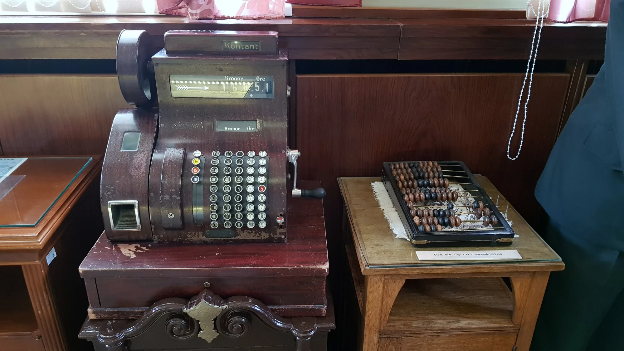 Старинная кассовая машина с надписями «Kronor» и «Öre» на деревянной подставке рядом со счётами бухгалтера С.Ю. Каломовой 1939 года.