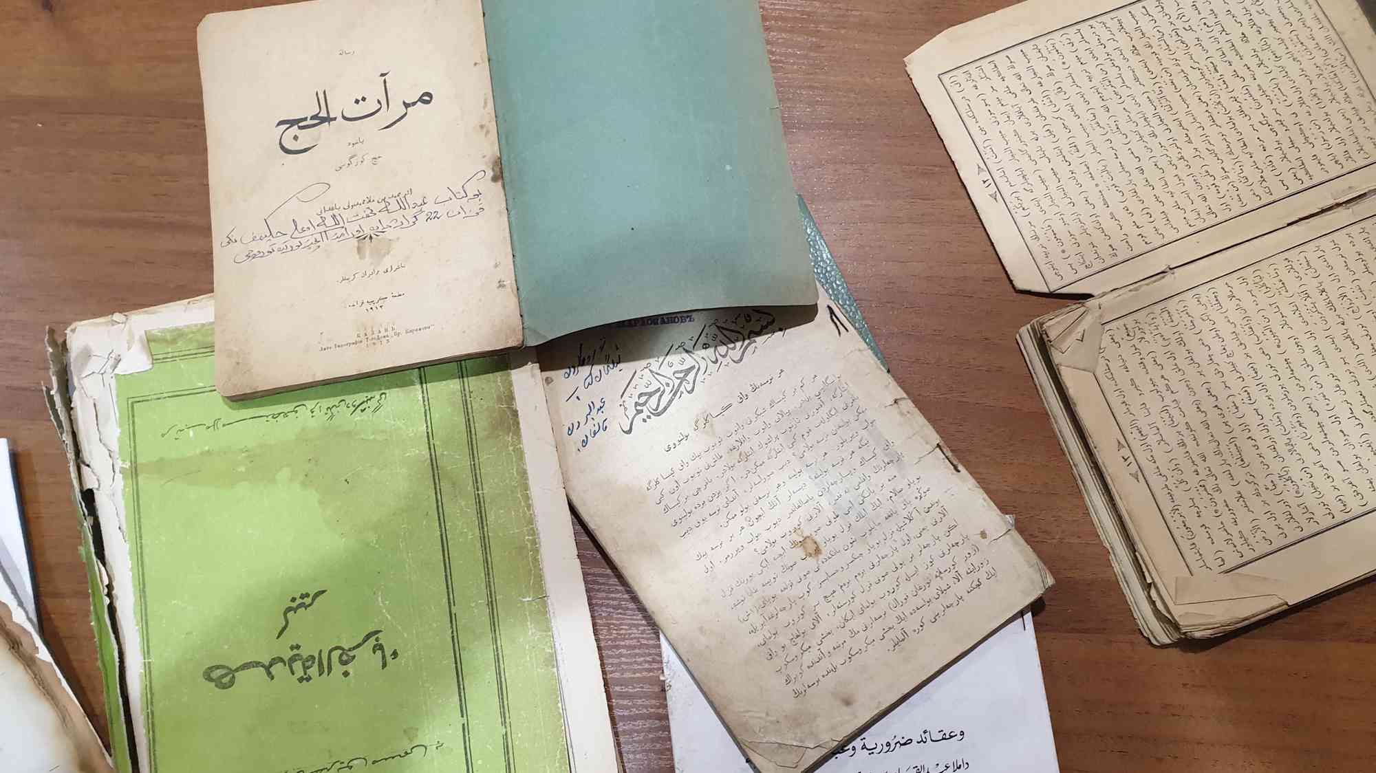 Старинные книги и рукописи на арабском и тюркских языках, включая «Марат аль-хадж» и «Хидаят аль-фарид», раскрыты на деревянном столе.