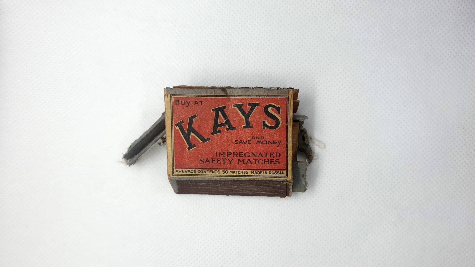 Старый деревянный коробок спичек «KAYS» с красной этикеткой: «BUY AT KAYS AND SAVE MONEY», «IMPREGNATED SAFETY MATCHES», «AVERAGE CONTENTS 50 MATCHES MADE IN RUSSIA» на белом фоне.