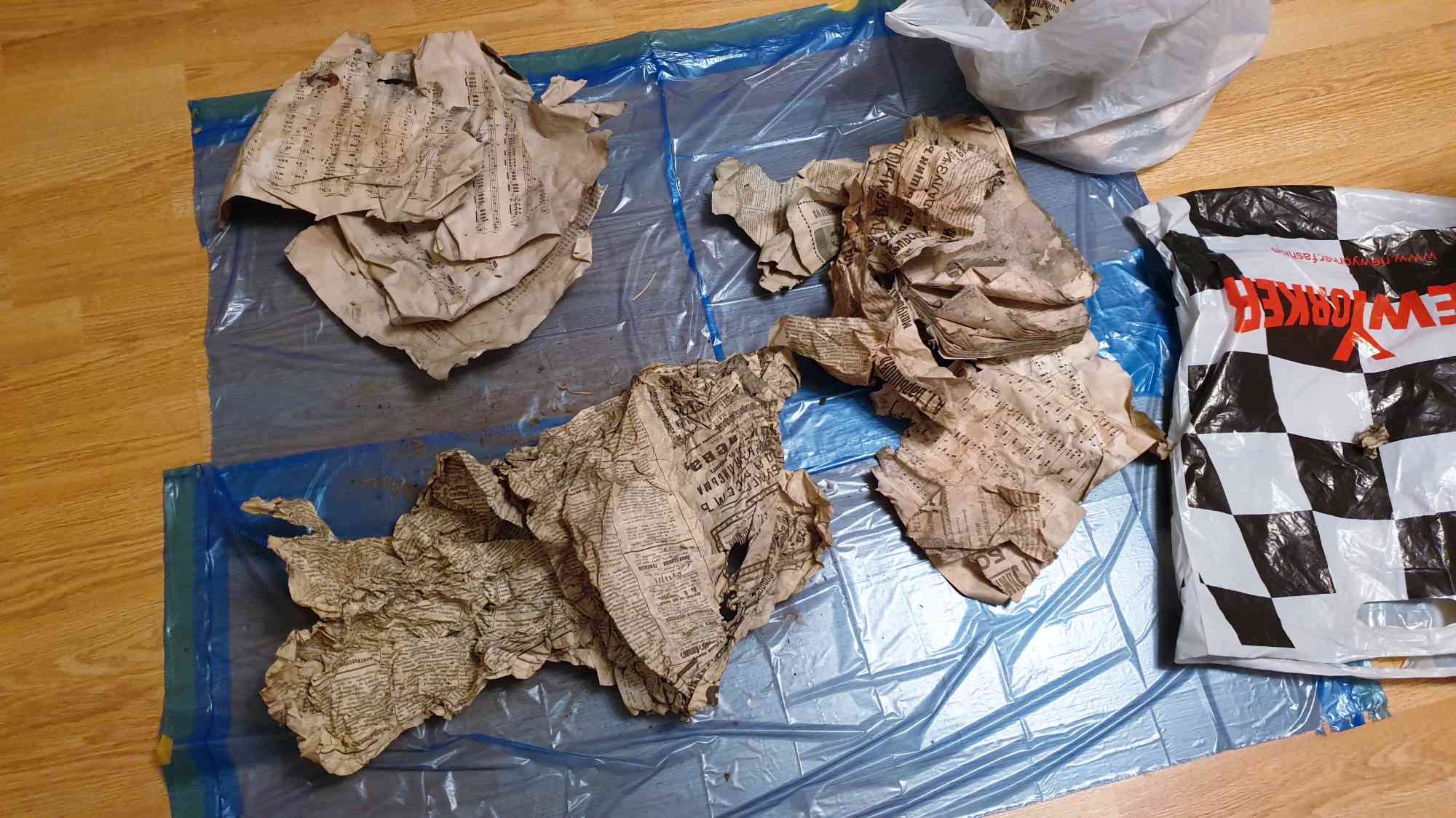 Смятые пожелтевшие страницы с нотами и текстом лежат на синой плёнке на полу рядом с пакетом «New Yorker».