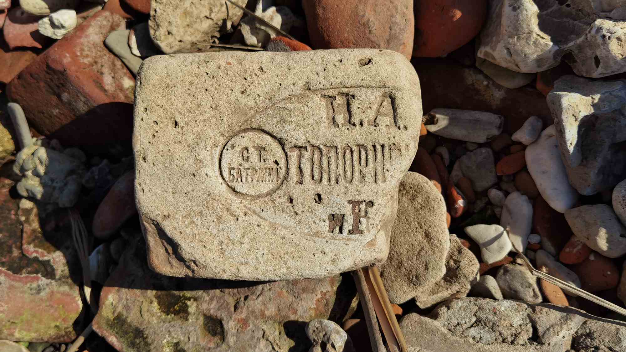 Старый кирпич с клеймом «П.А. ТОПОРКОВЪ» и круглым штампом «СТ. БАГРАМ» лежит среди камней и обломков на земле.