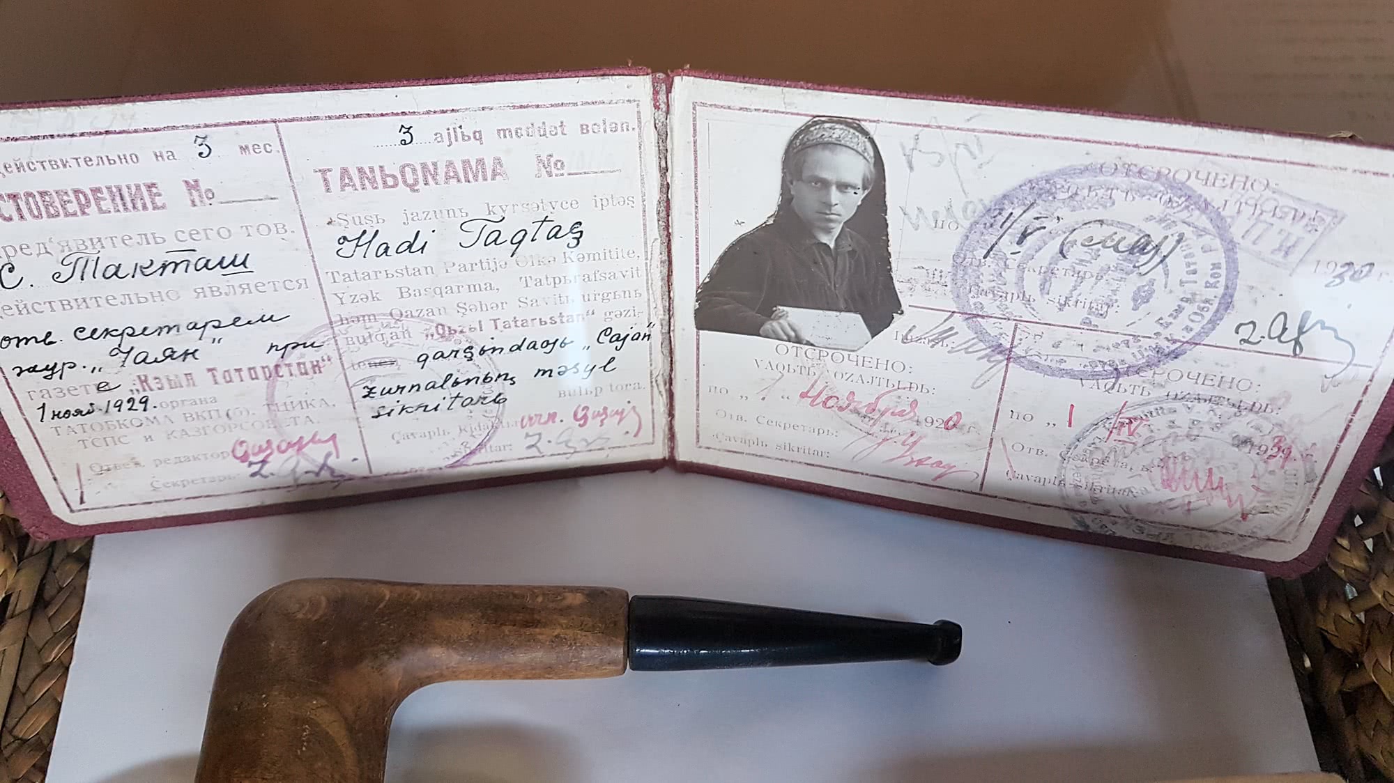 Открытое удостоверение журналиста с фото мужчины в головном уборе, подписью «Хаджи Тагташ» и печатями, рядом — деревянная трубка.