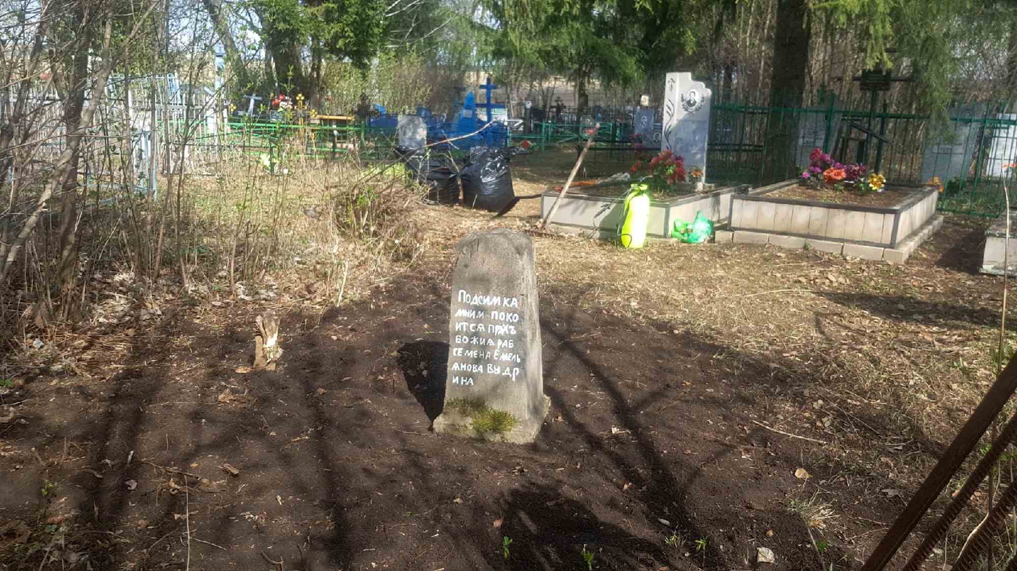 Старый каменный крест с надписью «Подсимика мним покоится прах раба Божия Семена Емельянова внука» на свежей могиле на кладбище.