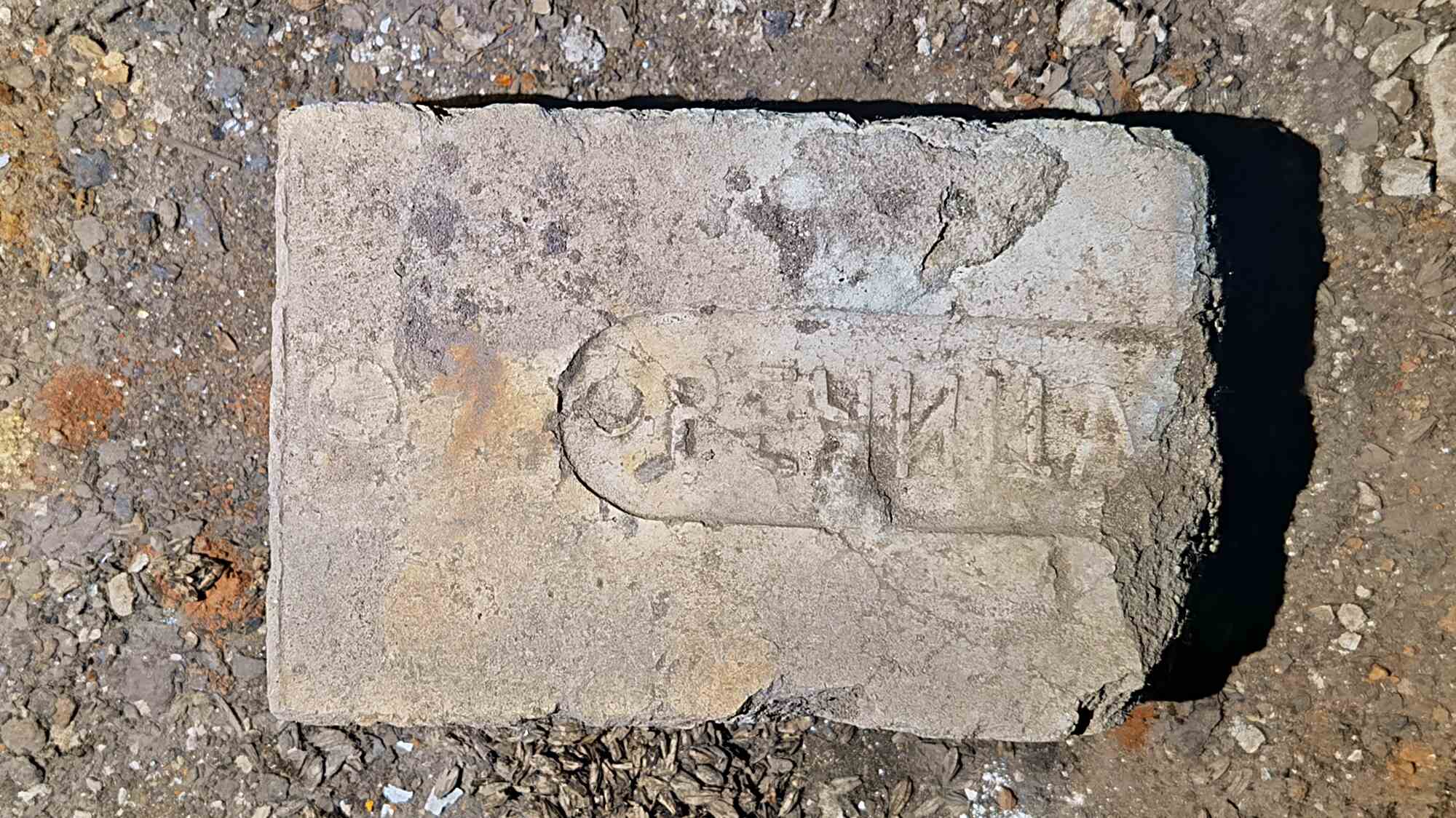 Старый бетонный блок с выцветшей надписью «ОПЕРАЦИЯ» и круглым логотипом, лежащий на земле среди щебня и мусора.