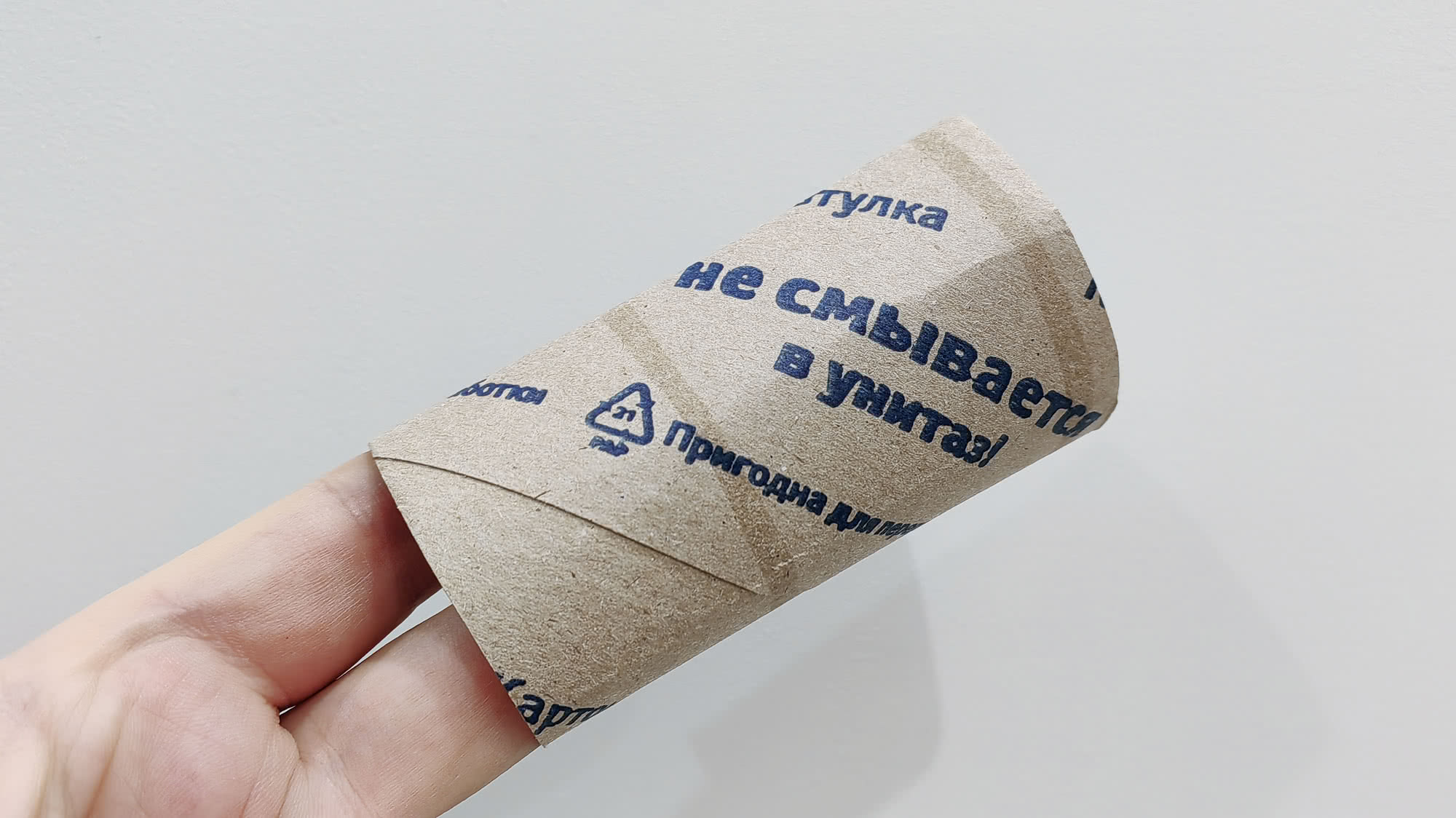 Рулон туалетной бумаги с надписью «туалетка не смывается в унитаз!» и знаком переработки, держится в руке на белом фоне.