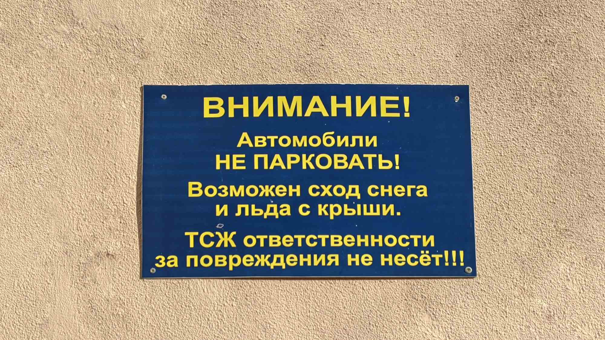 Синяя табличка с жёлтым текстом: «ВНИМАНИЕ! Автомобили НЕ ПАРКОВАТЬ! Возможен сход снега и льда с крыши. ТСЖ ответственности за повреждения не несёт!!!