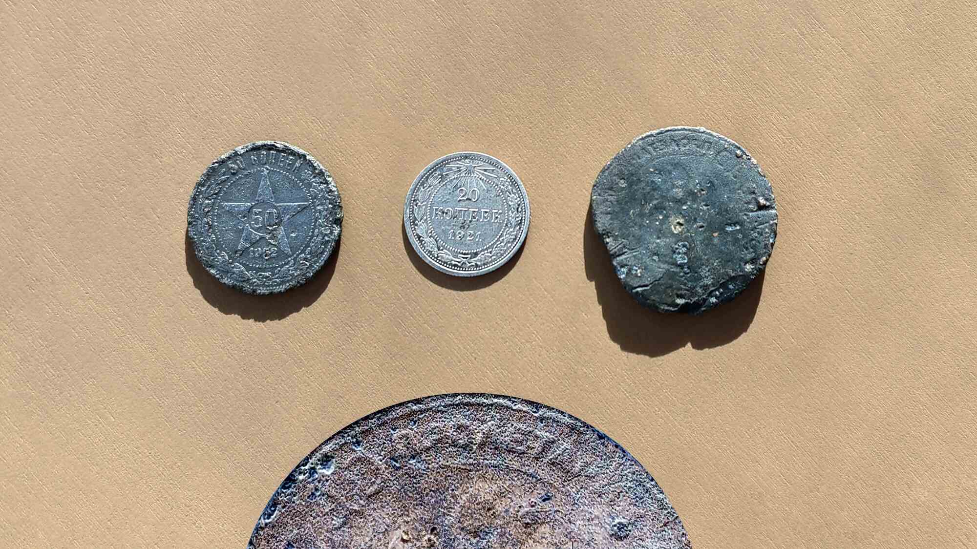 Четыре старые монеты на бежевом фоне: 50 копеек 1922 г. со звездой, 20 копеек 1921 г., потертая без надписей и крупная корродированная.