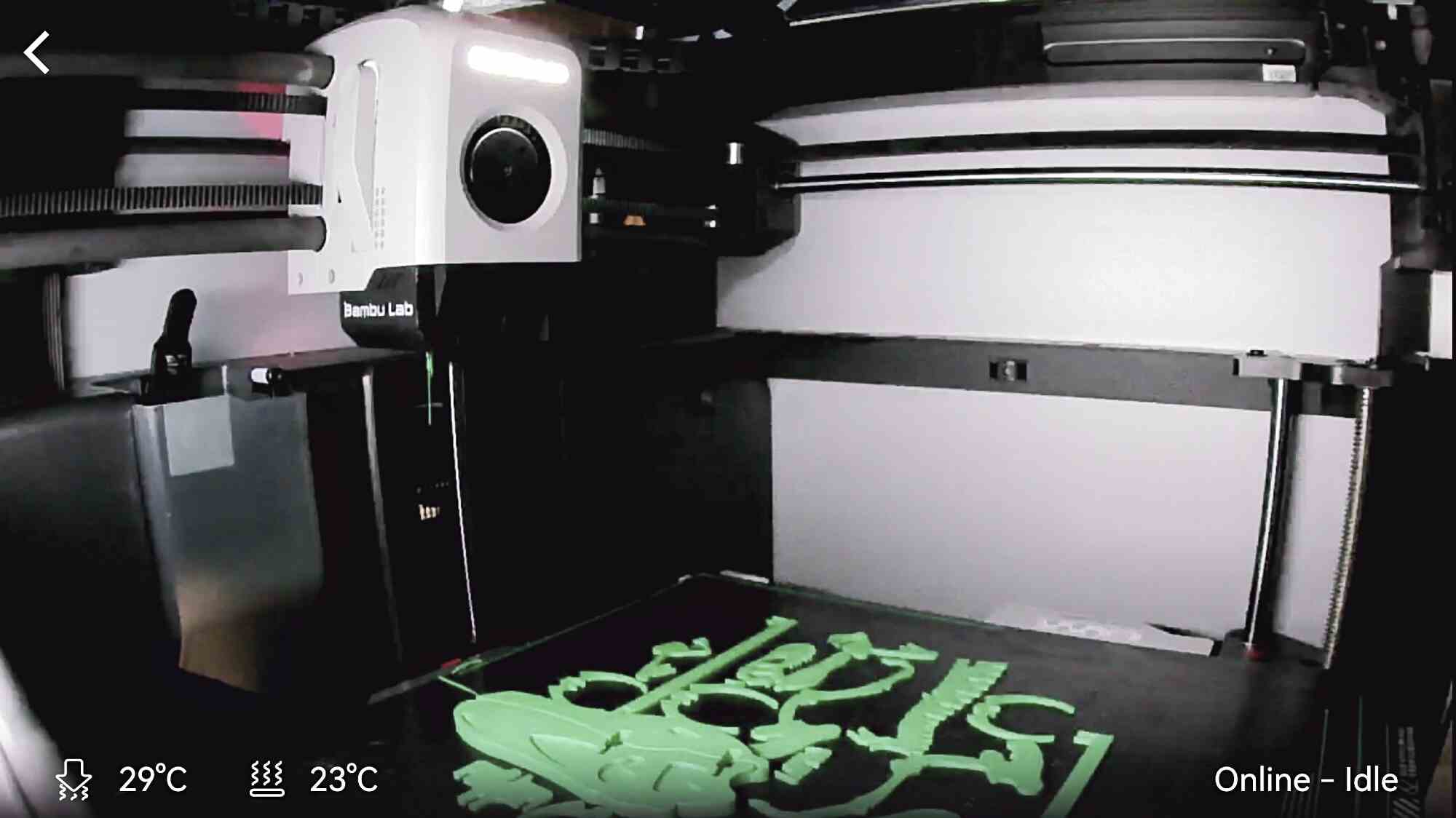 3D-принтер Bambu Lab печатает зелёные детали на чёрной платформе; на экране видны температуры 29°C и 23°C, статус «Online – Idle».