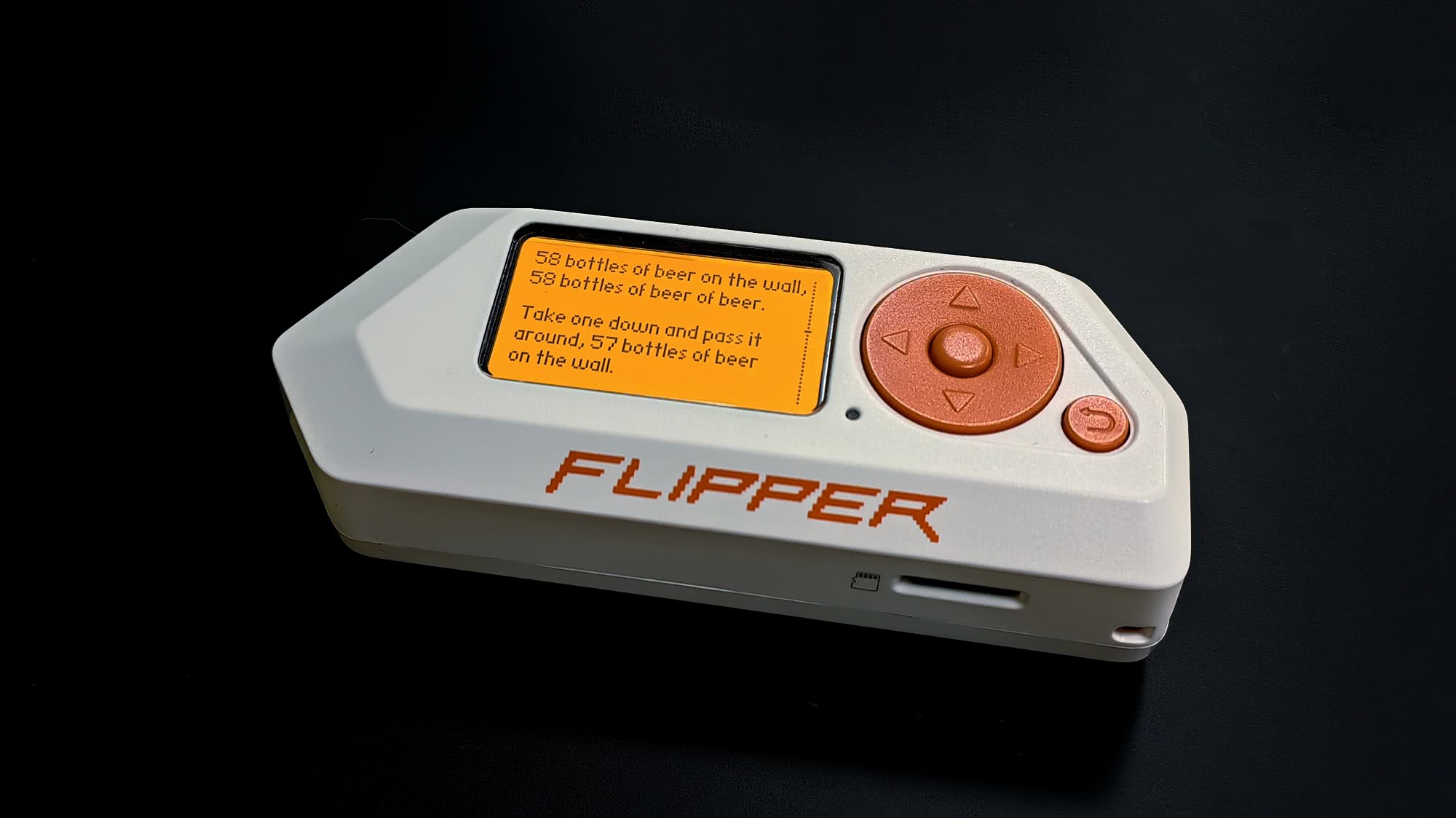 Белый многофункциональный инструмент Flipper Zero с оранжевым экраном, на котором отображается текст песни «58 bottles of beer on the wall», и оранжевыми кнопками управления.