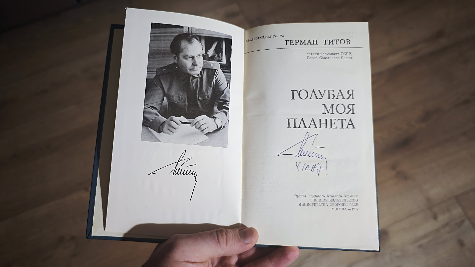 Открытая книга Германа Титова «Голубая моя планета» (1977) с автографом автора и датой 4.10.87 на титульном листе, рядом — фото космонавта в форме.