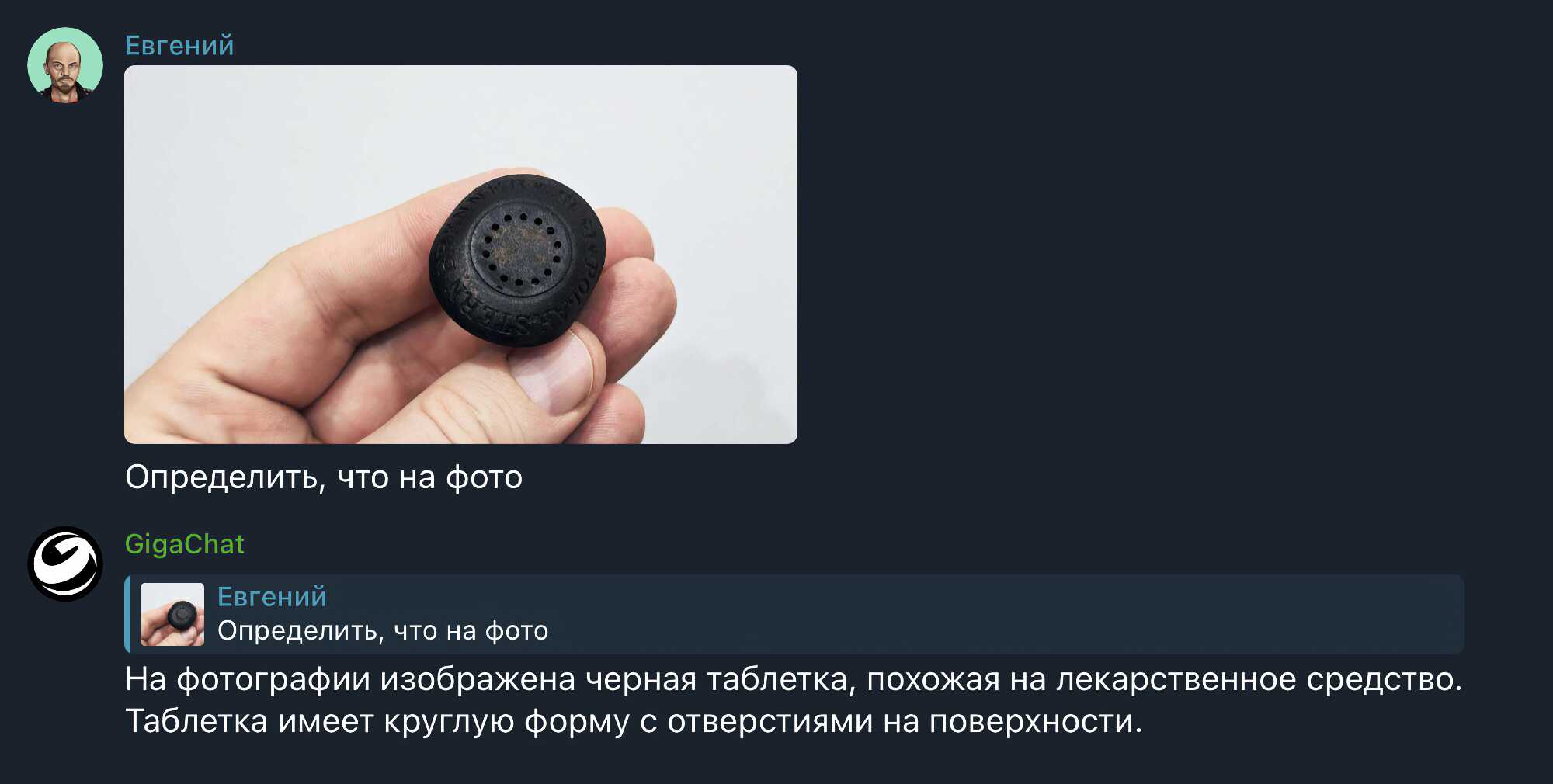 Рука держит чёрную круглую таблетку с отверстиями на поверхности, надпись на ней не читается.