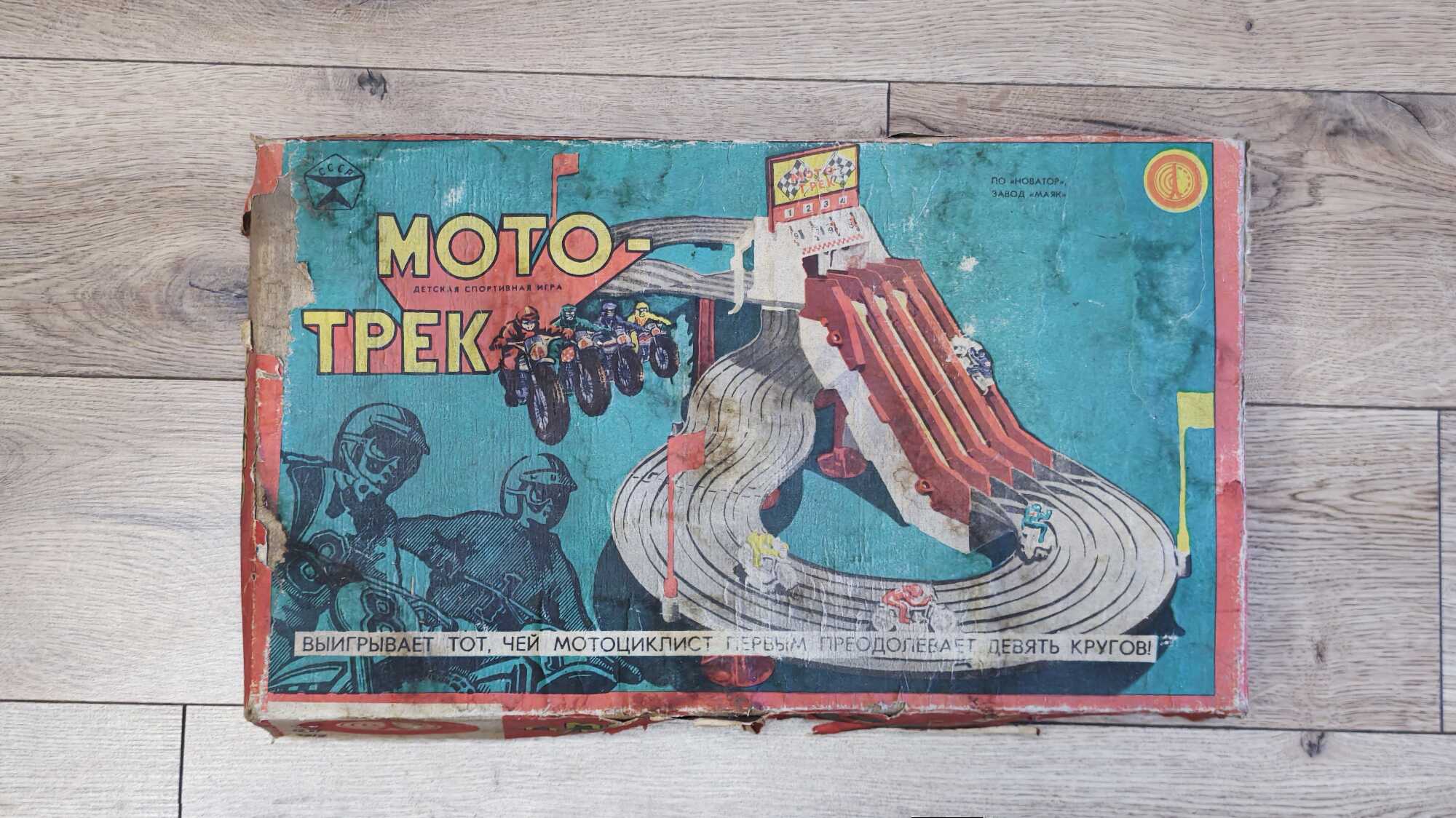 Ветхая коробка советской настольной игры «Мото-трек» с изображением мотогонщиков и трассы; надпись: «Выигрывает тот, чей мотоциклист первым преодолевает девять кругов!