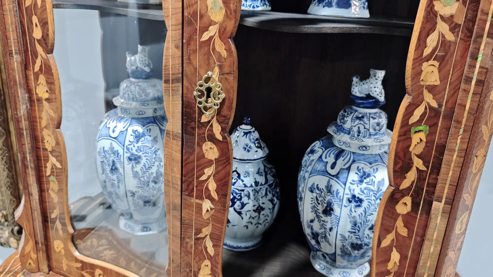 Три фарфоровых вазы с синим орнаментом и крышками, украшенными фигурками животных, стоят на полке деревянного шкафа с инкрустацией.