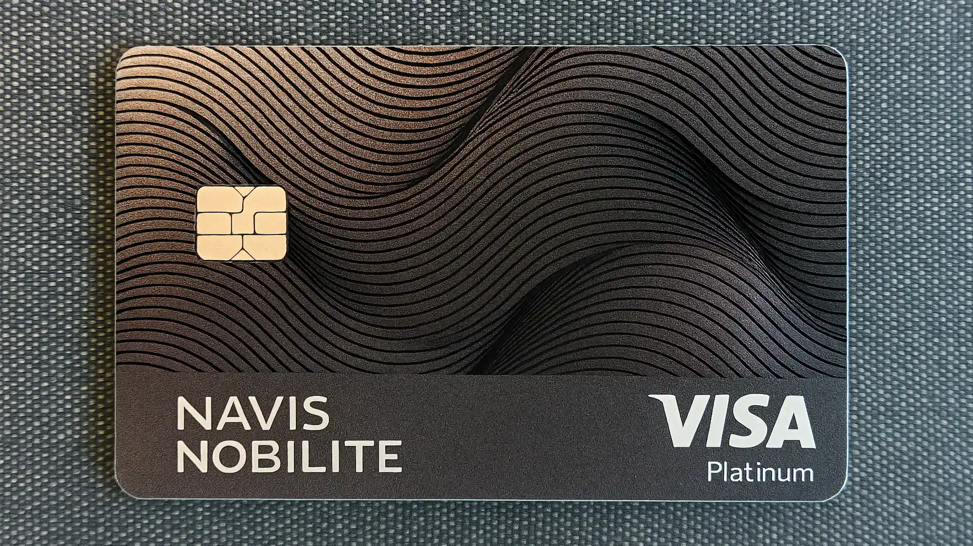 Банковская карта NAVIS NOBILITE VISA Platinum с волнистым узором и чипом на тёмном фоне.