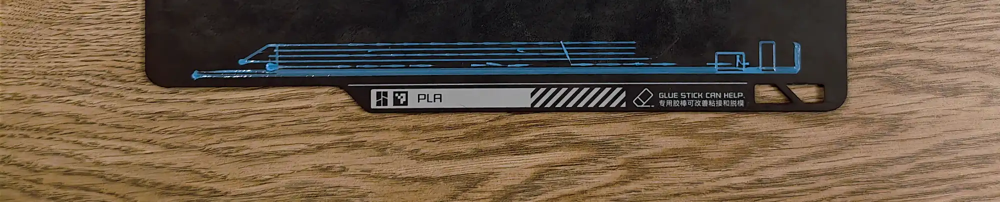 Чёрная 3D-печатная деталь с голубой схемой и надписью «PLA», а также текстом «GLUE STICK CAN HELP» и китайскими иероглифами о помощи клеящего стика при печати и снятии с платформы.