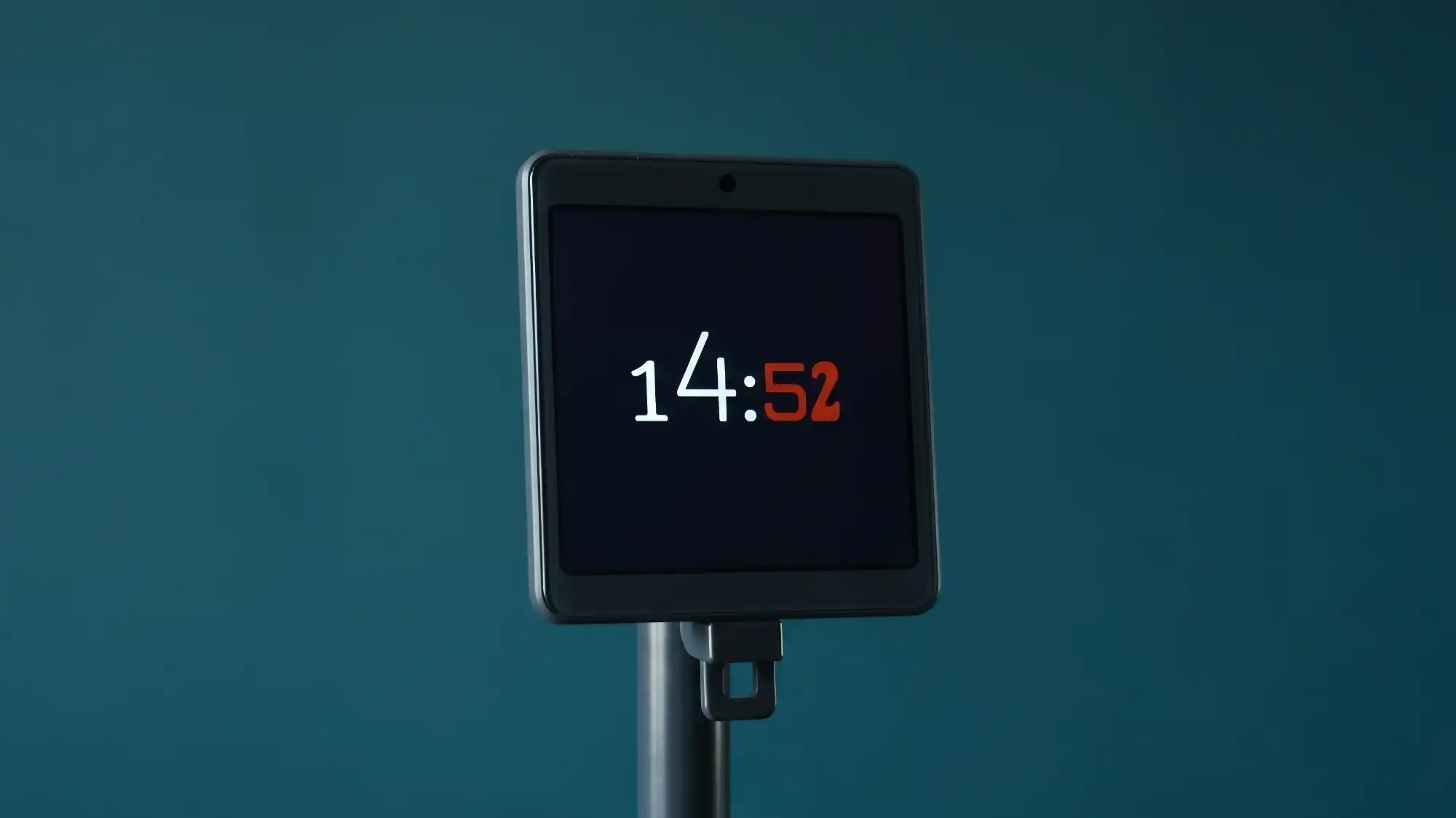 Цифровые часы на стойке показывают время 14:52, где цифры «14» белые, а «52» — красные, на тёмном фоне экрана.