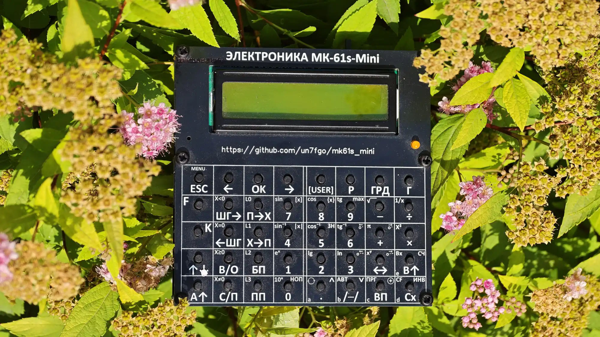 Калькулятор ЭЛЕКТРОНИКА МК-61s-Mini на фоне зелени. На корпусе URL: https://github.com/un7fg0/mk61s_mini